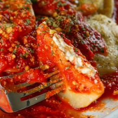 a fork is stuck into some ravioli and sauce on a plate with another pasta dish in the background