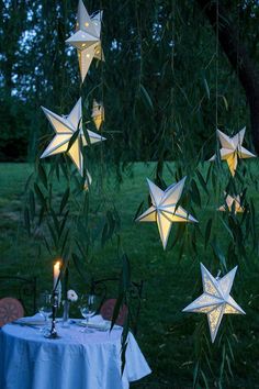 paper stars hanging from the branches of a tree at night with candles and tea lights