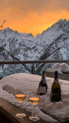 two glasses of wine are sitting on a table in front of the snow covered mountains