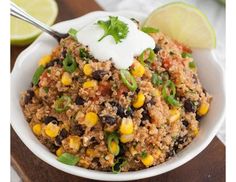 a white bowl filled with rice and vegetables next to lime wedges on a wooden table