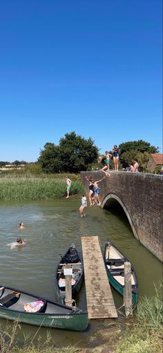 people are swimming in the water next to small boats and a bridge that is overpass