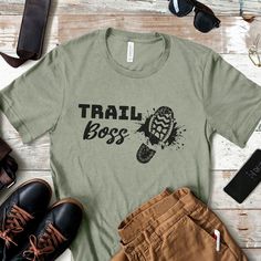 Trail Boss T-Shirt. Looking for a fun gift for a hiking friend or hike leader, a backpacker, or scout leader? Then check out this light and comfy hike lover tee. Bold and funny, it's perfect for wearing while leading hikes, as well as out and about to show who's the "boss" on your hiking adventures. Available in 12 cool colors for every season, this unisex tee looks great on men and women. HOW TO ORDER 1) Choose the shirt size you'd like in the 1st drop down menu. See below for help with Sizing Who's The Boss, Trail Boss, Hiking Adventures, Scout Leader, Mountain Adventure, Boss T Shirt, The Boss, Lovers Gift, Campfire