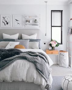 a bedroom with white walls and grey bedding, pillows and blankets on the bed