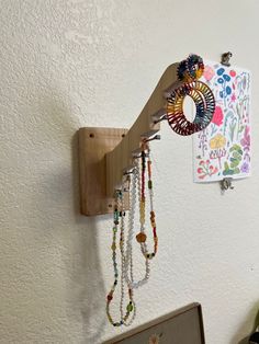 a wall mounted jewelry holder with beads hanging from it's side and a painting on the wall behind it