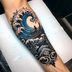 a man's arm with an ocean wave and boat tattoo on the left forearm