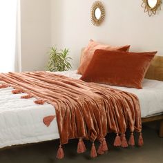 a bed with an orange blanket on top of it next to a mirror and potted plant