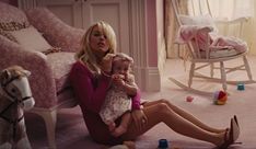 a woman sitting on the floor holding a baby next to a rocking chair and toy horse