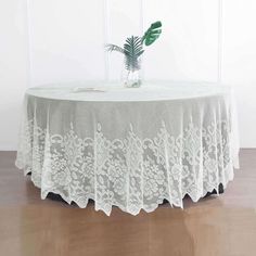 a round table with white lace on it and a green plant in the corner behind it