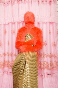 a pink and gold room with a woman in a fur coat on top of a chair