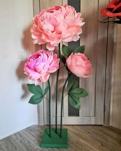 three large pink flowers in a green vase on a wooden floor next to a door