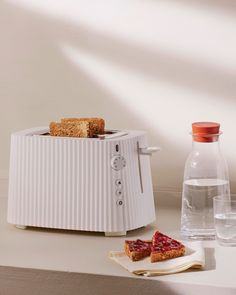 a toaster sitting on top of a counter next to two slices of bread and water