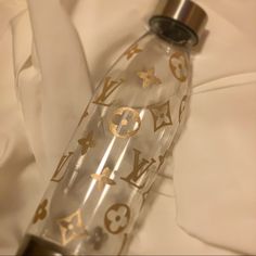 a clear bottle with gold lettering on it sitting on top of a white cloth covered bed