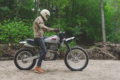 a man riding on the back of a motorcycle down a dirt road next to trees