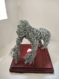 a sculpture of a dog made out of metal wire on a red wooden base in front of a white wall