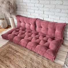 a pink futon couch sitting on top of a rug next to a white brick wall