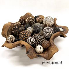 a wooden bowl filled with lots of different types of decorative balls on top of each other