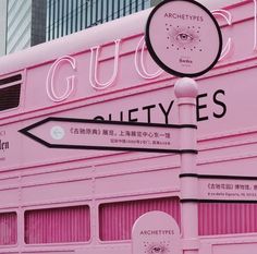 a pink double decker bus parked in front of a tall building with the word guco written on it