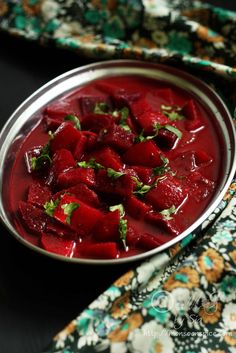 a metal bowl filled with beets on top of a floral table cloth next to a napkin