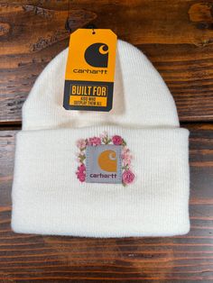 a white beanie hat with an orange and gray logo on it, sitting on top of a wooden table