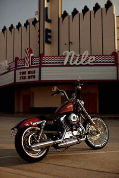 a red and black motorcycle parked in front of a movie theater with the marquee behind it