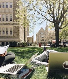 two people sitting on the grass with laptops and papers in front of them,