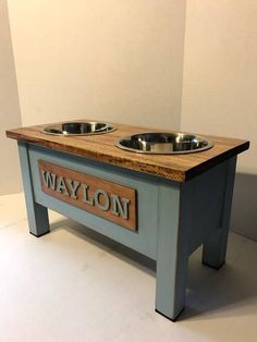 a dog bowl stand with two bowls on it and the words waylon engraved in wood