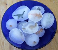 ice cubes in a blue bowl with small dinosaurs on them sitting on a wooden table