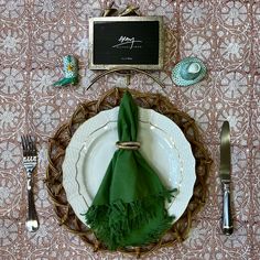 a place setting with green napkins, silverware and a chalkboard on the wall