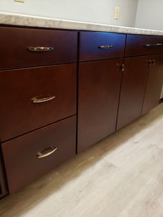 an empty kitchen with wooden cabinets and marble counter tops on the floor, in front of a white wall