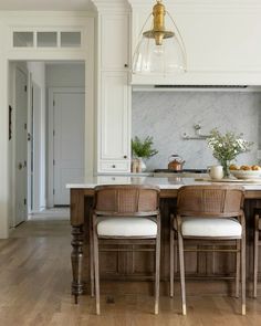 a kitchen with white cabinets and wooden flooring next to a dining room table filled with chairs