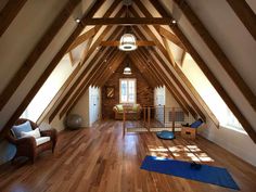 an open room with wooden floors and vaulted ceiling, yoga mat on the floor in front of window