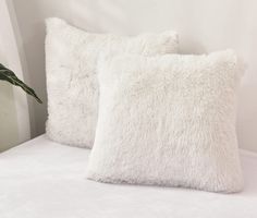 two white pillows sitting on top of a bed next to a green potted plant