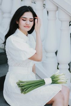 a woman in a white dress holding flowers sitting on the ground next to some stairs