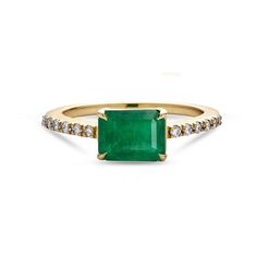 an emerald and diamond ring in yellow gold with diamonds on the sides, set against a white background