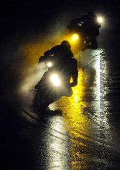 two motorcyclists riding in the rain at night with their headlights turned on