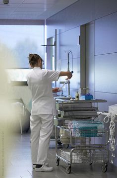 a woman in white scrubs is standing near a cart with medical supplies on it