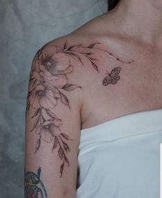 a woman wearing a white dress with flowers on her shoulder and butterfly tattoos on her arm