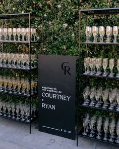 there are many wine glasses on display in front of a wall with greenery behind it