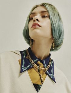 a woman with green hair wearing a scarf and gold chain necklace on top of her head