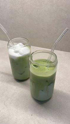 two glasses filled with green smoothie on top of a table