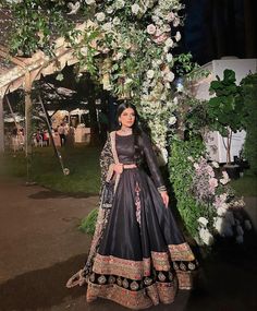 a woman in a black and gold dress standing under a floral covered archway at night