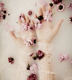 a person's hand with flowers on it in the middle of a bathtub