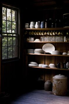 the shelves are full of dishes and plates in the dark room with open doors leading outside