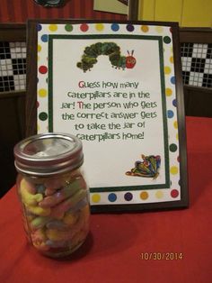 a jar filled with candy sitting on top of a table next to a sign that says guess how many caterpillars are in the jar