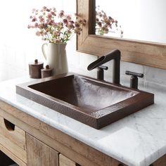 a bathroom sink sitting under a mirror next to a vase with flowers