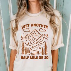 "Just Another Half Mile or So" Hiking T-Shirt Hit the trails in style with our "Just Another Half Mile or So" t-shirt, perfect for avid hikers and outdoor enthusiasts. Featuring a hand-drawn sketch of mountains and a winding hiking trail, this shirt embodies the spirit of adventure and the love for the great outdoors.   Product Details  Brand: Comfort Colors Material: 100% Cotton  Fit: Unisex sizing;  Pre-shrunk fabric ensures a consistently great fit;  Relaxed fit keeps the wearer comfy in both casual and semi-formal settings while the crew neckline delivers that classic, neat style which makes it perfect for accessorizing CARE INSTRUCTIONS: Machine wash cold, gentle cycle with like colors. Tumble dry low. Iron on a low setting if needed, avoiding the print. For further inquiries, please Hiking Graphic Tees, Take A Hike Shirt, Graphic Print Long Sleeve T-shirt For Hiking, Graphic Tee T-shirt With Crew Neck For Hiking, Funky Shirts, Hiking Tshirt, Casual Hiking T-shirt With Text Print, Adventure Outfit, Hiking Shirts