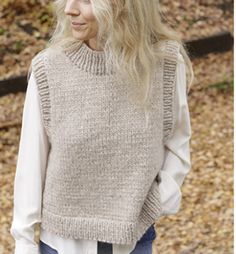 a woman standing in front of some trees wearing a sweater and jeans with her hands on her hips