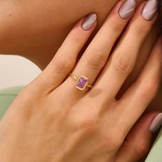 a woman's hand wearing a gold ring with a pink stone in the middle