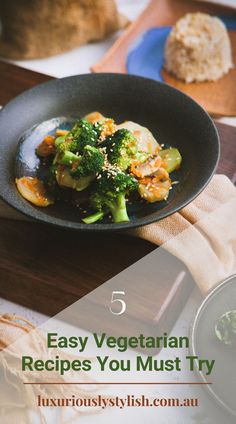 a black plate topped with broccoli and other food on top of a wooden table