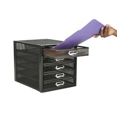 a person holding a purple piece of paper in front of a black file cabinet with drawers